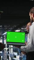 Vertical Army tech specialist in data center and coworkers using green screen laptop to troubleshoot military computer systems. Soldier and command center server room admins using chroma key notebook, camera A video