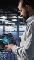 Vertical Technician holding laptop walking on server farm platform, doing AI machine learning automatization. Data center programmer using notebook, doing maintenance using artificial intelligence, camera A video