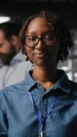 Vertical Happy technician next to server hub engineering team colleagues reviews AI diagnostics. Cheerful african american woman working in data center to maintain operational reliability, camera B video