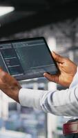 Vertical Close up of data center programmer looking at code debugging tools running on tablet. Server farm IT professional checking machine learning script automating tasks, camera B video