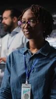 Vertical Happy technician next to server hub engineering team colleagues reviews AI diagnostics. Cheerful african american woman working in data center to maintain operational reliability, camera A video