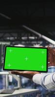 Vertical Close up of IT experts using chroma key device to analyze neural networks outputs. Data center admin uses green screen tablet next to colleague reviewing AI visualization in blurry background video