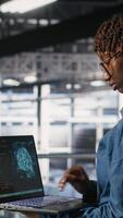 Vertical System administrators in data center monitoring AI LLM visualization. African american server farm coworkers overseeing rigs powering machine learning processes, camera B video