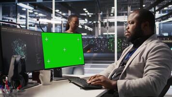 Data center programmer working on green screen desktop PC, updating storage infrastructure. IT specialist using mockup computer in server hub workspace filled with networking tech, camera A video