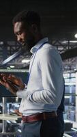 Vertical Technician walks in data center, doing maintenance tasks on tablet, ensuring optimal performance. IT expert reviewing diagnostics and applying patches to server hub gear, improving stability, camera A video