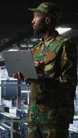 Vertical Army information technology specialist in data center troubleshooting military computer systems and networks using laptop. Soldier in command center server room using notebook, camera A video