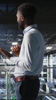 Vertical Admin on data center industrial platform analyzing infrastructure performance outputs on tablet. Server room employee doing job tasks, finetuning mainframes configurations, camera A video
