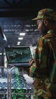 Vertical Soldier in server room uses geospatial data to support evacuation during emergency operations. Military data center personnel in uniform coordinating disaster response logistics using laptop, camera A video