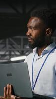Vertical Engineers in data center using laptop to monitor neural network LLM visualization. Coworkers on server hub industrial platform overseeing server clusters powering machine learning processes, camera B video