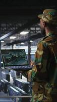 Vertical Military technician in data center monitoring warfare drone telemetry on laptop dashboard. IT specialist in army server room using tactical interface on notebook to support aerial operations, camera A video