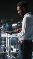 Vertical Server hub teamworking IT experts visualizing large language model architecture using notebook. Data center system administrators on industrial platform collaborating on tasks using laptop video