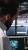 Vertical Military server room IT professionals using AI LLM tech on laptop to review network performance. Army operators manage hardware systems supporting mission critical connectivity, camera B video