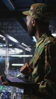 Vertical Army IT specialist in data center using laptop to defend networks against cyber threats. Military command center admin using notebook to identify potential intrusions or malicious activities, camera A video