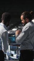 Vertical Data center workers cooperating, doing maintenance on rigs handling AI processing tasks. Server hub admins doing brainstorming, managing storage arrays supporting deep learning technology, camera A video