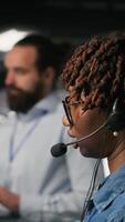 Vertical Data center worker on industrial platform speaks in headset microphone while overseeing maintenance on AI rigs below. Admin uses tablet to coordinate deep learning system tasks with team, camera B video