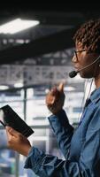 Vertical Server hub IT expert monitors systems, doing tech support, guiding users through troubleshooting steps. African american technician providing remote diagnostics using headset mic, camera B video