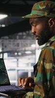 Vertical Soldier in server room uses geospatial data to support evacuation during emergency operations. Military data center personnel in uniform coordinating disaster response logistics using laptop, camera B video