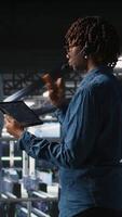 Vertical Server hub IT expert monitors systems, doing tech support, guiding users through troubleshooting steps. African american technician providing remote diagnostics using headset mic, camera A video