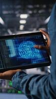 Vertical Close up of server farm admin using tablet to do infrastructure AI machine learning automatization. Data center software developer doing maintenance using artificial intelligence, camera A video