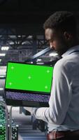 Vertical Technicians on data center industrial platform analyzing performance outputs on green screen laptop. Server hub engineering team finetuning server rig configurations using mockup notebook, camera A video
