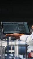 Vertical Close up of programmer swiping on tablet display in data center, doing maintenance tasks, ensuring optimal performance. IT expert checks code on device, applying patches to improve stability, camera A video