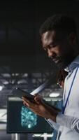 Vertical Engineer walking on data center industrial platform, performing system maintenance. IT professional using tablet to do upgrades, resolving bugs and enhancing infrastructure stability, camera A video