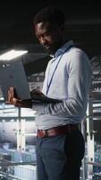 Vertical Engineers in data center using laptop to monitor neural network LLM visualization. Coworkers on server hub industrial platform overseeing server clusters powering machine learning processes, camera A video
