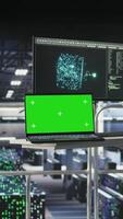 Vertical Mockup notebook in data center displaying neural network activity. Automated infrastructure green screen laptop workstation on industrial platform inside server hub showing AI machine learning scripts video
