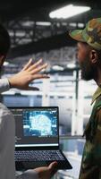 Vertical Military technicians in secure data center use laptop to monitor artificial intelligence systems. Army operators in server hub ensuring stable infrastructure for machine learning operations, camera B video