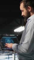 Vertical Data center team leader and worker reviewing performance dashboards of AI equipment rigs. Server room supervisor oversees programmer examining machine learning algorithms on screen, camera B video