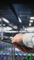 Vertical Close up of data center software developer doing maintenance tasks on tablet, ensuring optimal performance. Worker reviewing diagnostics and applying patches to server hub equipment, camera A video