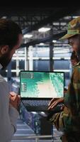 Vertical Drone operators in military data center supervising autonomous flight systems through laptop interface. Teamworking army IT experts doing live drone tracking using notebook, camera A video