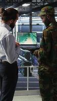 Vertical Military IT specialists in server hub using laptop scanner tools to oversee battlefield during warfare. Army data center admins doing transmission analysis and live UAV system monitoring, camera A video