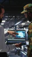 Vertical Military technicians in secure data center use laptop to monitor artificial intelligence systems. Army operators in server hub ensuring stable infrastructure for machine learning operations, camera A video