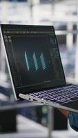 Vertical Close up of admin in data center using laptop to monitor neural network LLM visualization. Server hub IT expert overseeing rigs powering machine learning processes using notebook, camera B video