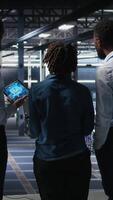 Vertical Software developers in data center monitoring AI LLM visualization. Server farm teamworking colleagues doing brainstorming, overseeing rigs powering machine learning processes, camera A video