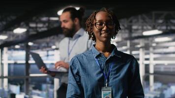 Portrait of smiling data center admin next to coworkers running diagnostics on equipment to identify errors. Happy woman next to IT experts working to prevent failure and minimize downtime, camera B video