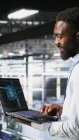 Vertical Programmer and colleague in data center reviewing AI LLM visualizations on laptop. IT teamworking coworkers analyze neural network performance outputs to ensure stable infrastructure operations video