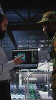 Vertical Military operator and IT expert in army data center using AI on laptop to manage autonomous defense systems. Soldier and programmer using AI for strategic threat detection, camera A video