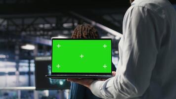 Close up of server room worker using green screen laptop next to colleague reviewing AI LLM visualization. Data center IT professional chroma key notebook to monitor AI systems, camera B video