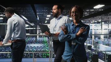 Portrait of smiling data center admin next to coworkers running diagnostics on equipment to identify errors. Happy woman next to IT experts working to prevent failure and minimize downtime, camera A video