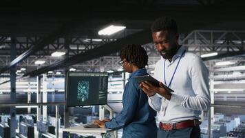 Engineer walking on data center industrial platform, performing system maintenance. IT professional using tablet to do upgrades, resolving bugs and enhancing infrastructure stability, camera B video
