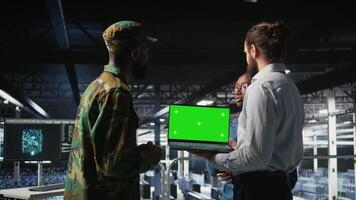 Army tech specialist in data center and coworkers using green screen laptop to troubleshoot military computer systems. Soldier and command center server room admins using chroma key notebook, camera A video