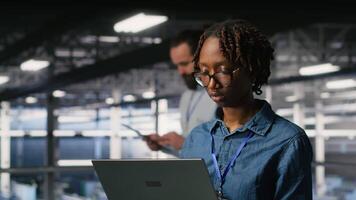 Happy woman in data center doing maintenance tasks on laptop, ensuring optimal performance. Engineering team reviewing diagnostics and applying patches to server room, improving stability, camera B video