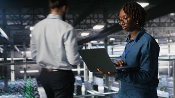 Data scientist in server farm reviewing neural network code and LLM visualization dashboards. IT expert walking on data center industrial platform, monitoring AI system performance, camera B video