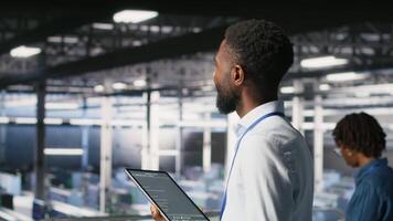 Data center programmer checking lines of code and colleague reviewing AI LLM visualizations. IT experts analyze neural networks outputs to ensure stable infrastructure operations, using tablet video