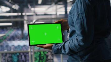 Close up of IT experts using chroma key device to analyze neural networks outputs. Data center admin uses green screen tablet next to colleague reviewing AI visualization in blurry background video