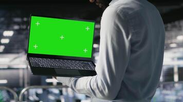 Technicians on data center industrial platform analyzing performance outputs on green screen laptop. Server hub engineering team finetuning server rig configurations using mockup notebook, camera B video