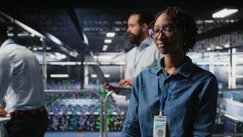 Happy technician next to server hub engineering team colleagues reviews AI diagnostics. Cheerful african american woman working in data center to maintain operational reliability, camera A video