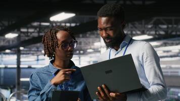 Data center system administrators using laptop to review AI LLM visualizations. African american IT specialists use device to analyze neural networks outputs, ensuring stable gear operations video